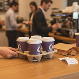 Hand holding Zeropac 4-cup carrier with coffee cups in cafe setting