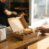Customer receiving takeout box with grilled skewers and fries