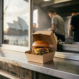 Deluxe burger in Zeropac box at waterfront cafe with city landmark view