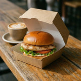 Grilled burger in Zeropac kraft box on cafe table with coffee nearby