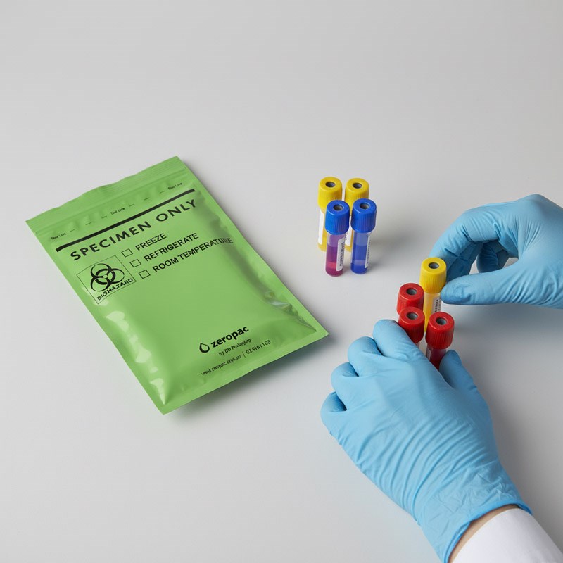 A pair of blue-gloved hands organizes several colored-cap test tubes next to a green "zeropac" specimen bag on a neutral surface.