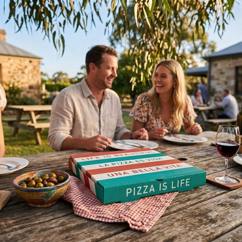 Couple dining outdoors at vineyard with pizza boxes and wine glasses